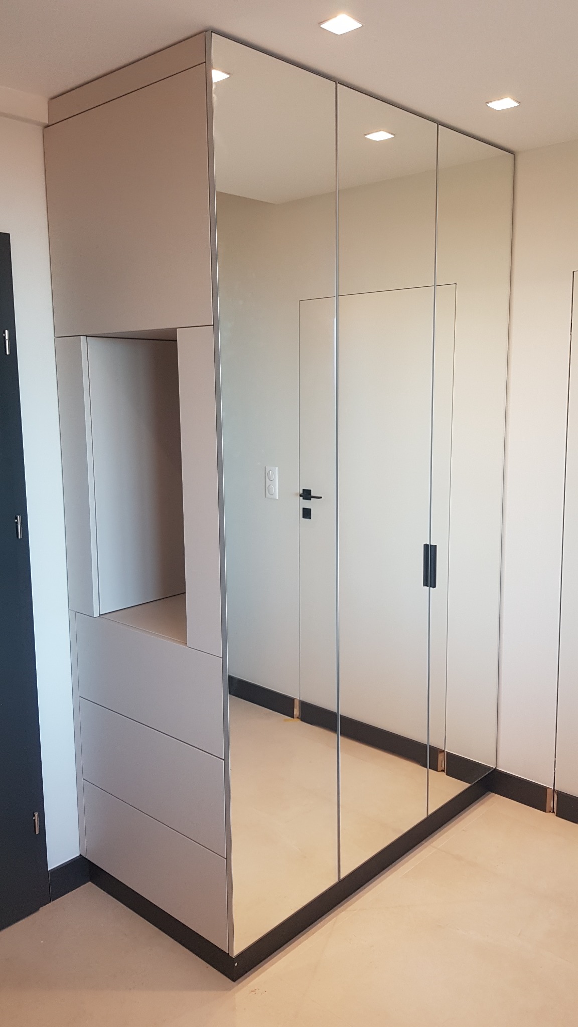 Jasnoszara zabudowa wnęki z lustrzanymi drzwiami przesuwnymi, widoczne szuflady i otwarta półka, minimalistyczny design.