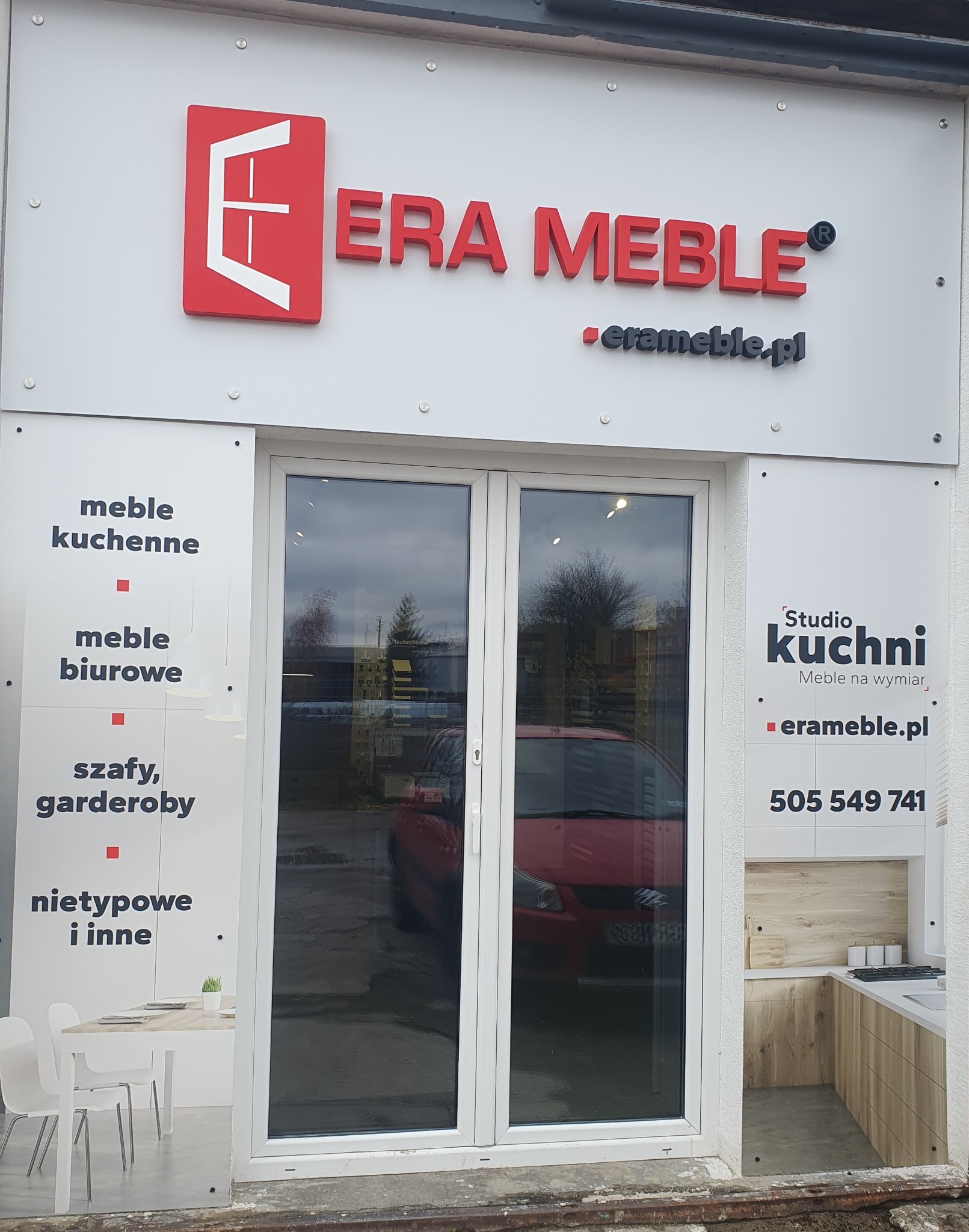 Fasada budynku z logo i nazwą firmy Era Meble, oferującej meble kuchenne, biurowe, szafy i garderoby na wymiar, widoczny numer telefonu i adres strony internetowej.