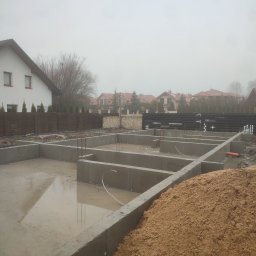 BOHDAN LUKIANIV - Zalane wodą betonowe fundamenty domu jednorodzinnego w trakcie budowy, widoczny stos piasku i zabudowa sąsiedzka w tle.