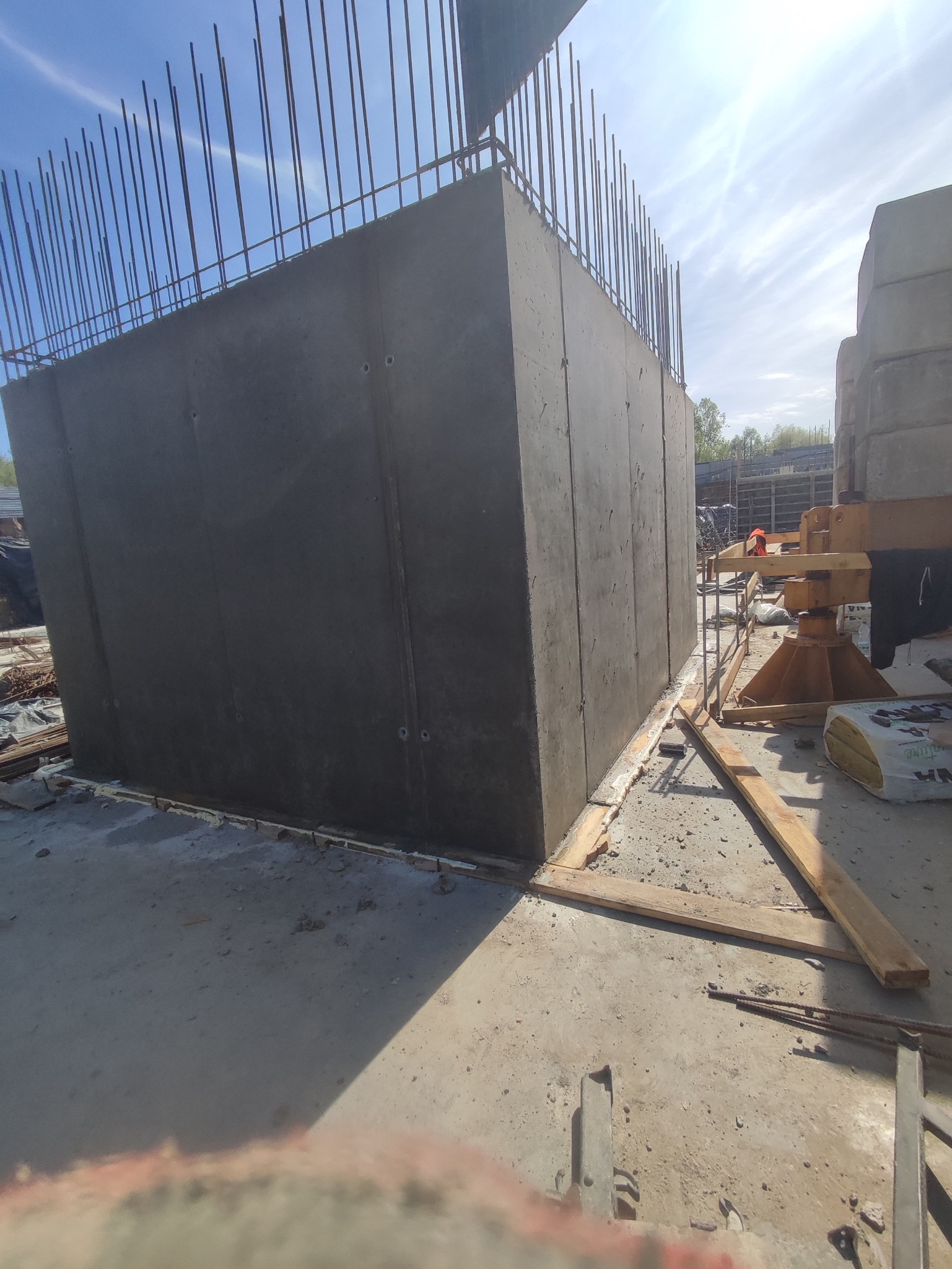 Świeżo wylany, szary betonowy blok z wystającymi prętami zbrojeniowymi na budowie w słoneczny dzień.