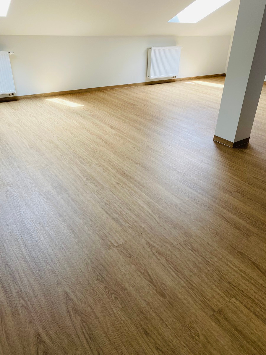 Jasne panele podłogowe ułożone w nowym pokoju z grzejnikami i filarem, widok z góry.