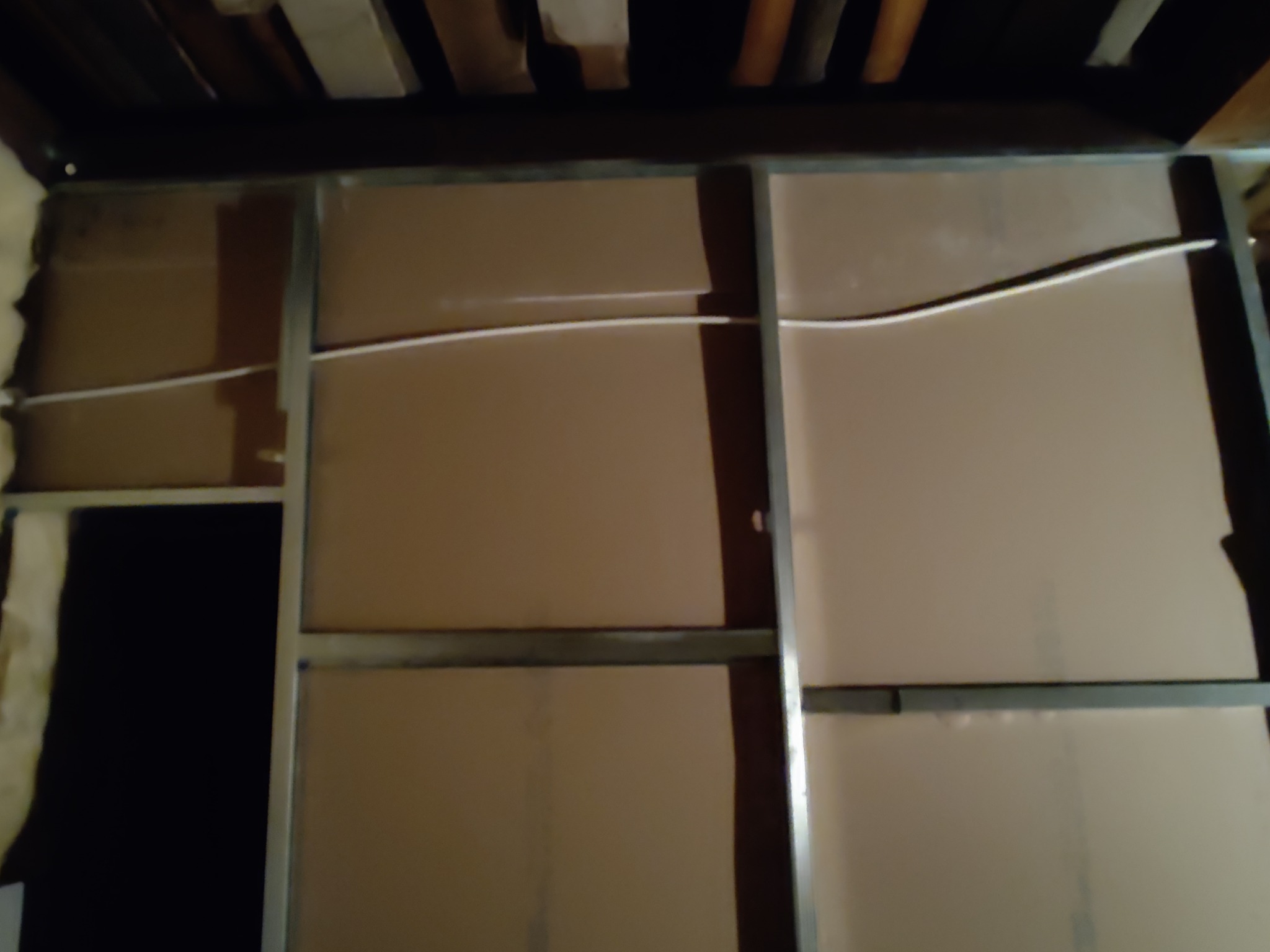 Wnętrze w trakcie prac wykończeniowych, widoczne płyty kartonowo-gipsowe na metalowym stelażu, biały kabel elektryczny biegnący wzdłuż ściany, ocieplenie z wełny mineralnej w szczelinie.