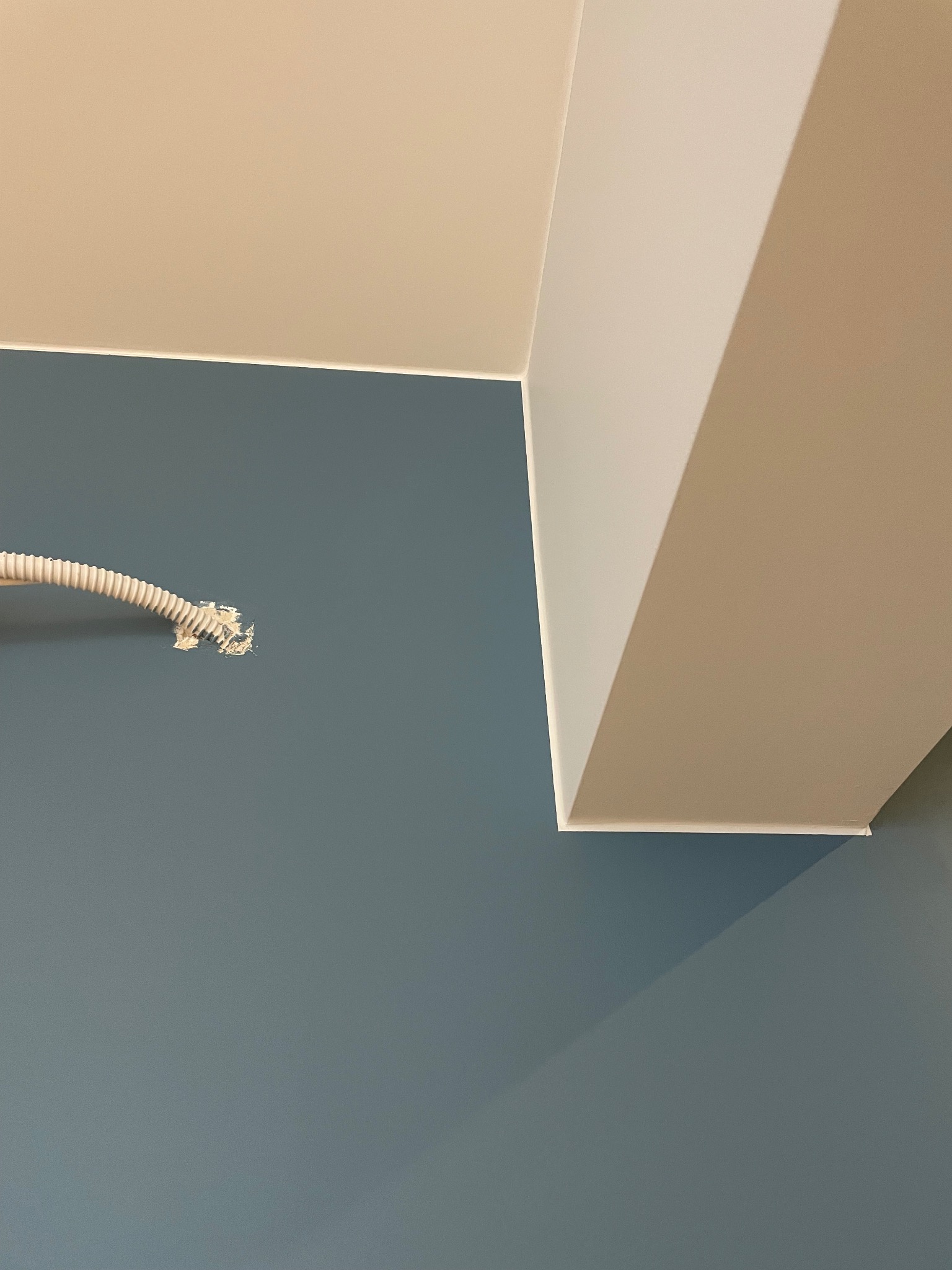 Niebieska ściana z fragmentem białego sufitu i wystającą rurką instalacyjną z widocznymi resztkami zaprawy.