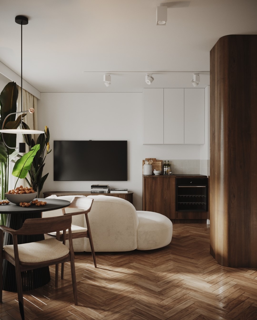 Jasne wnętrze mieszkania z parkietem w jodełkę, okrągłym stołem z owocami, kremową sofą i zabudową kuchenną z drewnianymi szafkami.