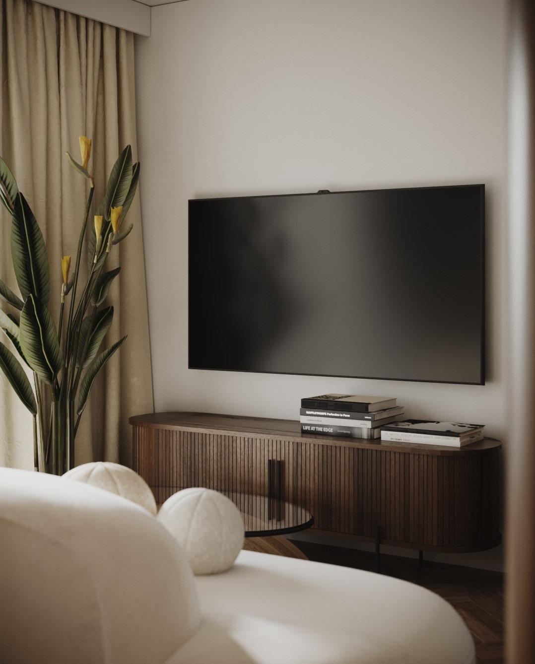 Minimalistyczny salon z telewizorem na ścianie, drewnianą komodą, rośliną w doniczce i okrągłymi poduszkami na białej sofie.