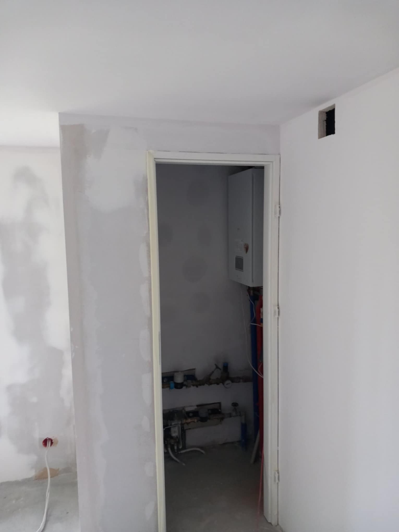 Wnętrze łazienki w trakcie prac wykończeniowych, widoczny zamontowany piec gazowy, instalacja wodna i kanalizacyjna oraz ściany przygotowane do malowania