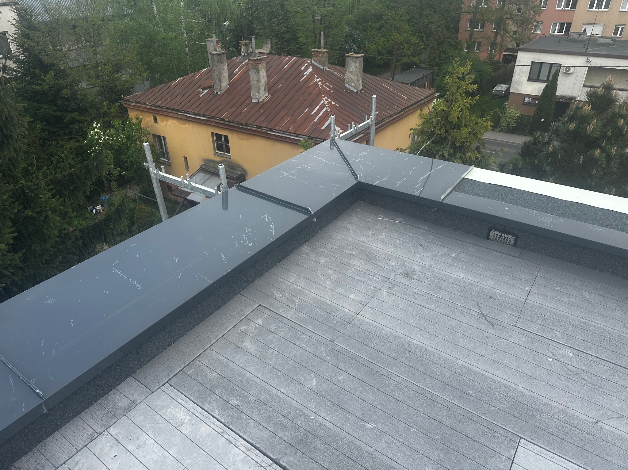Szare, nowoczesne wykończenie dachu płaskiego z detalami imitującymi marmur, widok z góry na tle zabudowy miejskiej i zieleni.