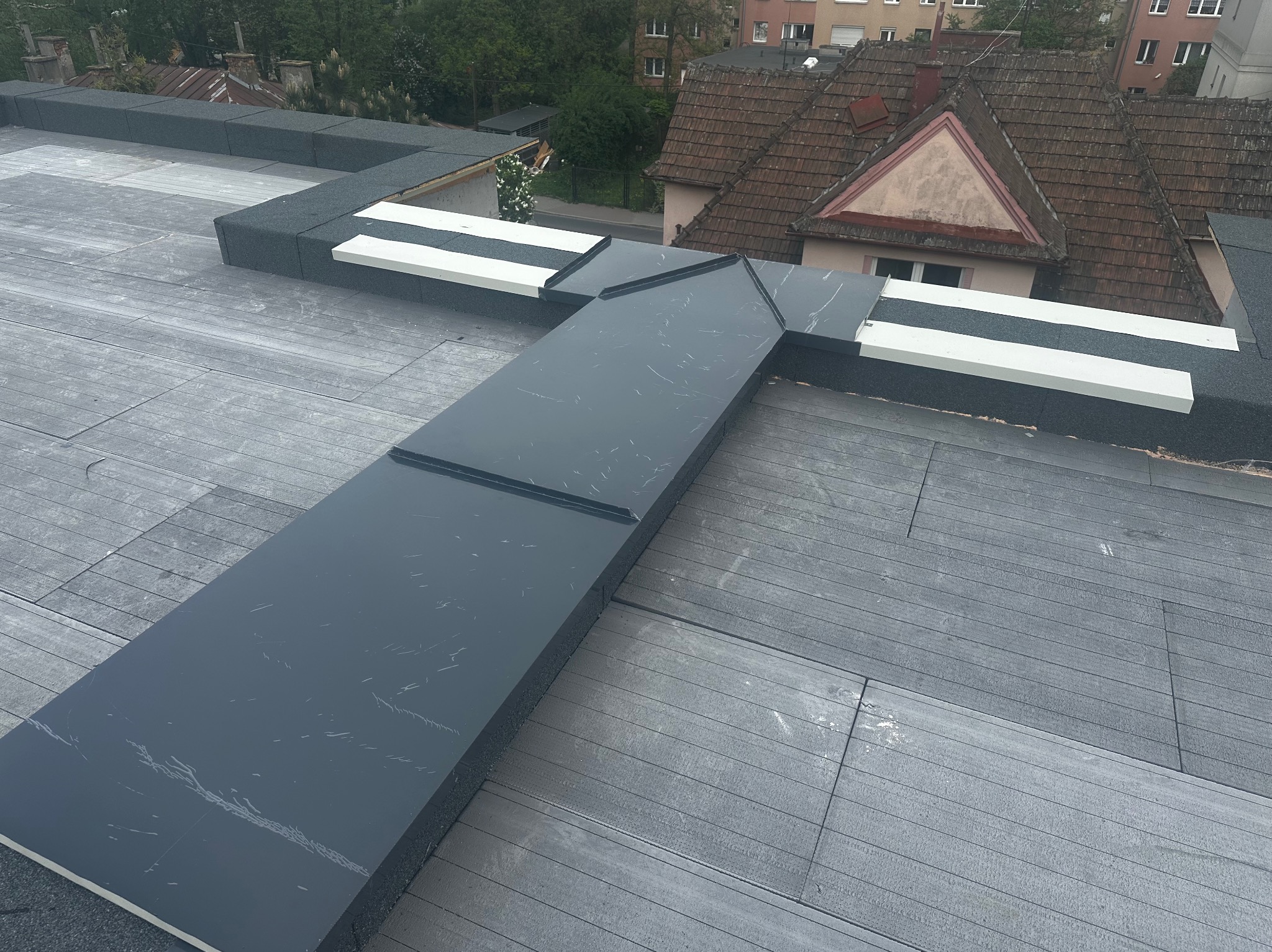 Nowoczesne wykończenie dachu płaskiego z elementami blachy w kolorze grafitowym i białym. Widok z góry na gotową konstrukcję.