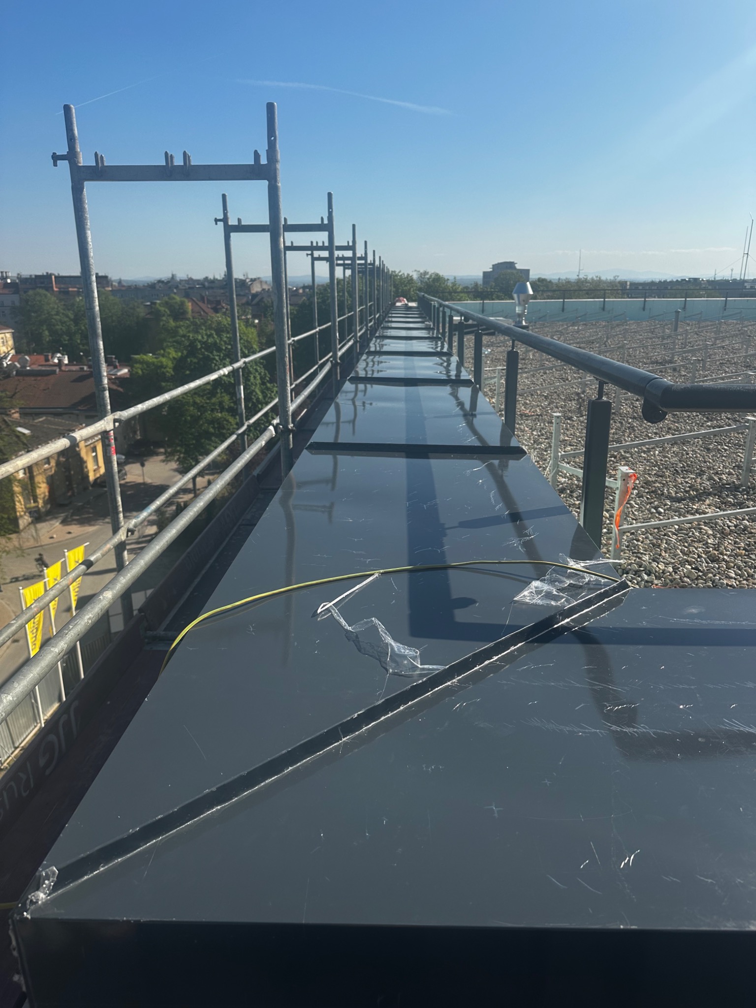 Nowe obróbki blacharskie na dachu budynku w Krakowie, zabezpieczone folią ochronną. Widoczne rusztowania i panorama miasta w tle. Prace dekarskie.