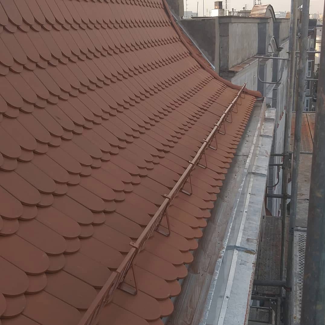 Dachówka karpiówka w kolorze ceglastym na dachu budynku z widoczną rynną i elementami konstrukcyjnymi. Ujęcie z góry, podkreślające wzór ułożenia.