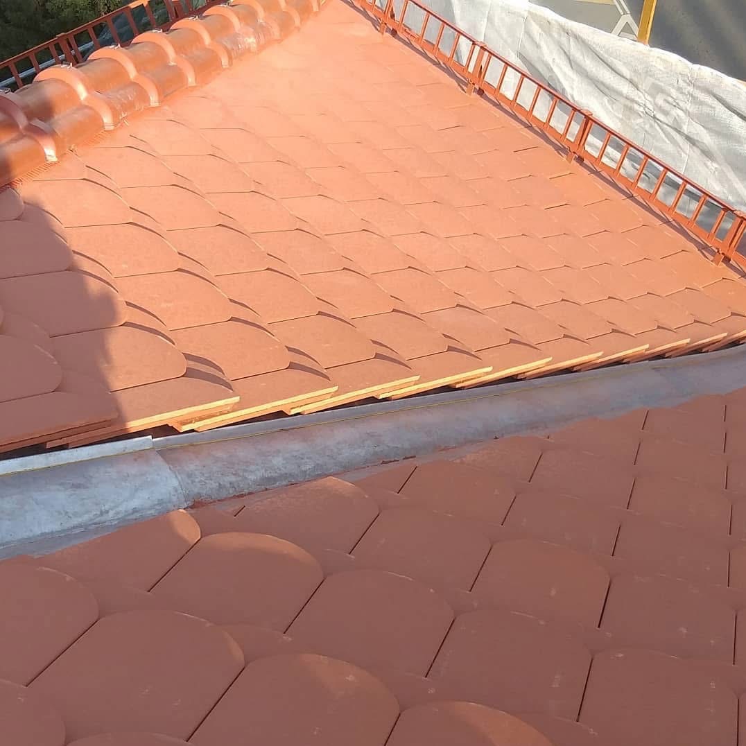 Czerwona dachówka ceramiczna ułożona na dachu, widok z góry. Widoczne detale konstrukcji i zabezpieczenia na krawędzi dachu. Dachówka w kształcie łuski.