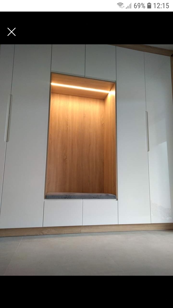 Biała szafa wnękowa z drewnianym wnęką z podświetleniem LED i szarą poduszką na siedzisku.