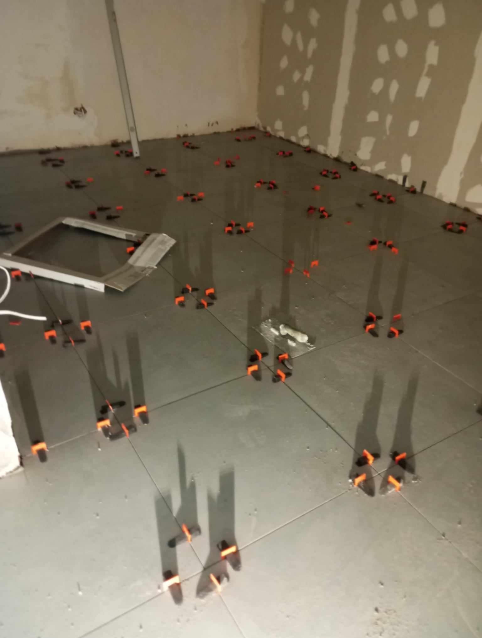 Układanie szarych płytek podłogowych z użyciem poziomowania klipsami w trakcie prac w Poznaniu, widoczne narzędzia i przygotowana ściana.