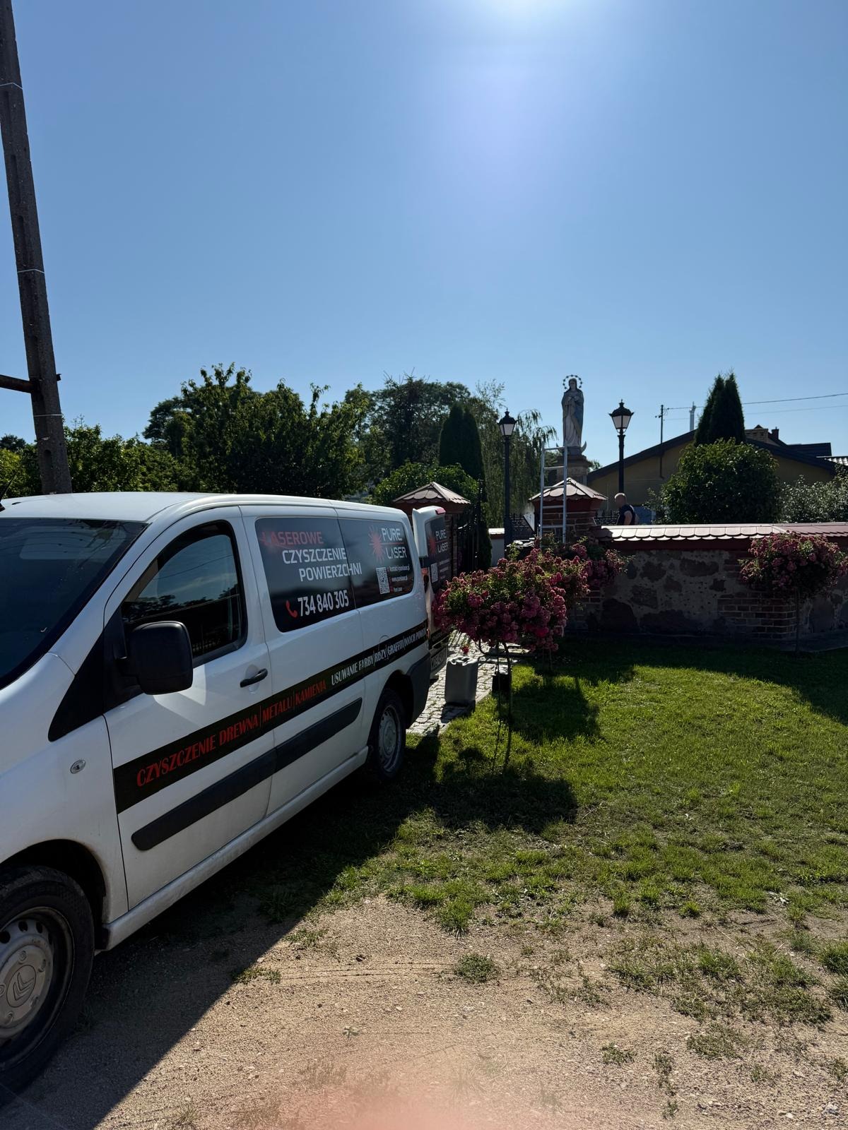 Biały van z napisem 'laserowe czyszczenie powierzchni' zaparkowany na tle kapliczki. Specjalizacja: czyszczenie drewna, metalu, kamienia, usuwanie farby, rdzy i graffiti.