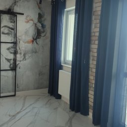 Ruslan Iva - Nowoczesne wnętrze z przesuwnymi drzwiami loftowymi z grafiką, marmurową podłogą, ścianą z cegły i zasłonami w odcieniach granatu, widok na balkon.