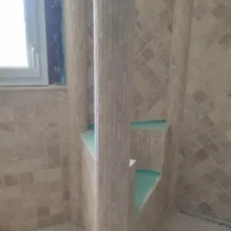 Wnętrze łazienki w Tczewie w trakcie wykańczania, z kolumnami obłożonymi mozaiką i przygotowaną wnęką, widoczne płytki w odcieniach beżu i brązu.