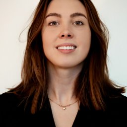 Piotr Wojnarowski - Portret uśmiechniętej brunetki z brązowymi oczami, w czarnej bluzce i delikatnym złotym naszyjniku na białym tle. Ujęcie centralne od klatki piersiowej w górę.