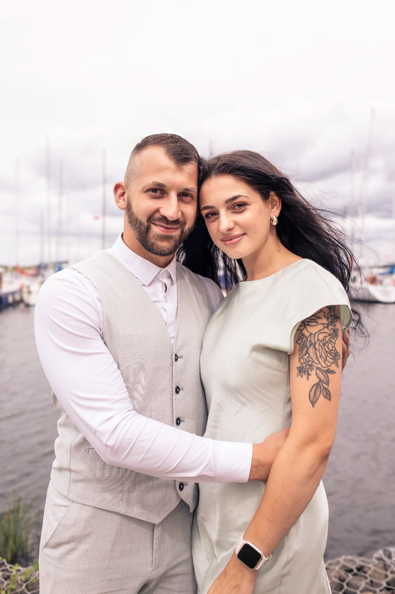 Zakochana para w Szczecinie pozuje na tle przystani jachtowej. Kobieta ma tatuaż na ramieniu, mężczyzna ubrany jest w elegancką kamizelkę.