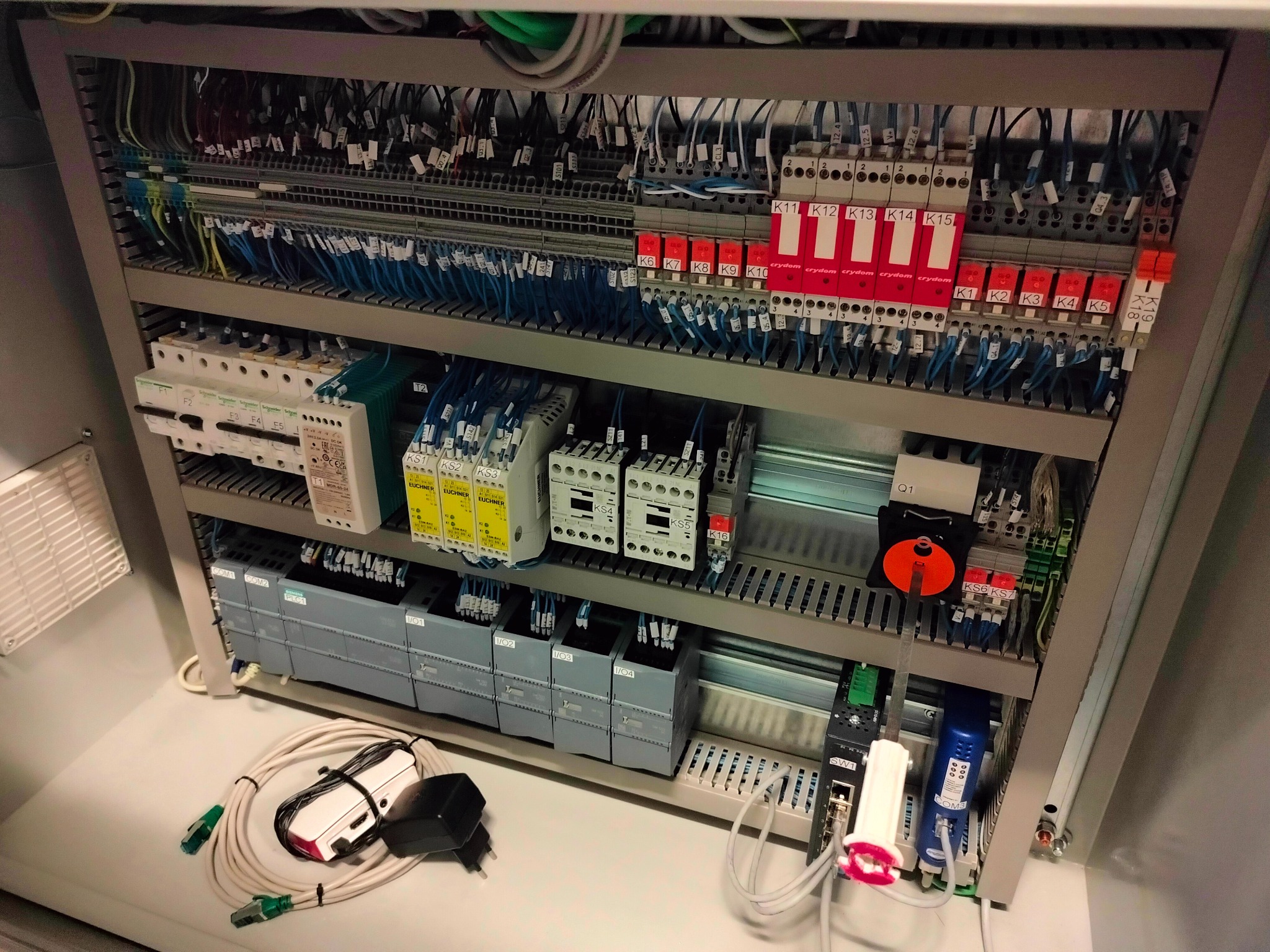 Wnętrze szafy sterowniczej z widocznymi modułami PLC Siemens, przekaźnikami Crydom, złączkami, okablowaniem i testerem sieciowym leżącym na dnie szafy.