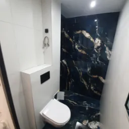 Wąska łazienka po remoncie z toaletą podwieszaną, biało-czarnymi płytkami imitującymi marmur i ukrytą spłuczką.