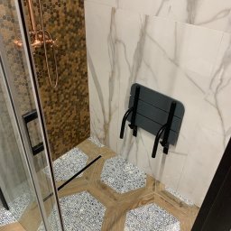 Kwadrat - Nowoczesna kabina prysznicowa z mozaiką heksagonalną w odcieniach brązu, marmurowymi płytkami ściennymi, drewnopodobną podłogą w kształcie heksagonów z niebieskim wzorem i składanym siedziskiem.