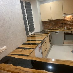 Kwadrat - Nowoczesna kuchnia z blatem z drewna i żywicy epoksydowej, ściana z cegły, jasne szafki i szara ściana z fakturą.