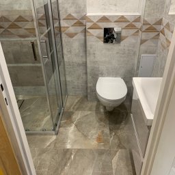 Kwadrat - Nowoczesna łazienka z kabiną prysznicową, wiszącą toaletą i umywalką w zabudowie, wykończona płytkami imitującymi marmur z dekoracyjnym pasem z geometrycznym wzorem.