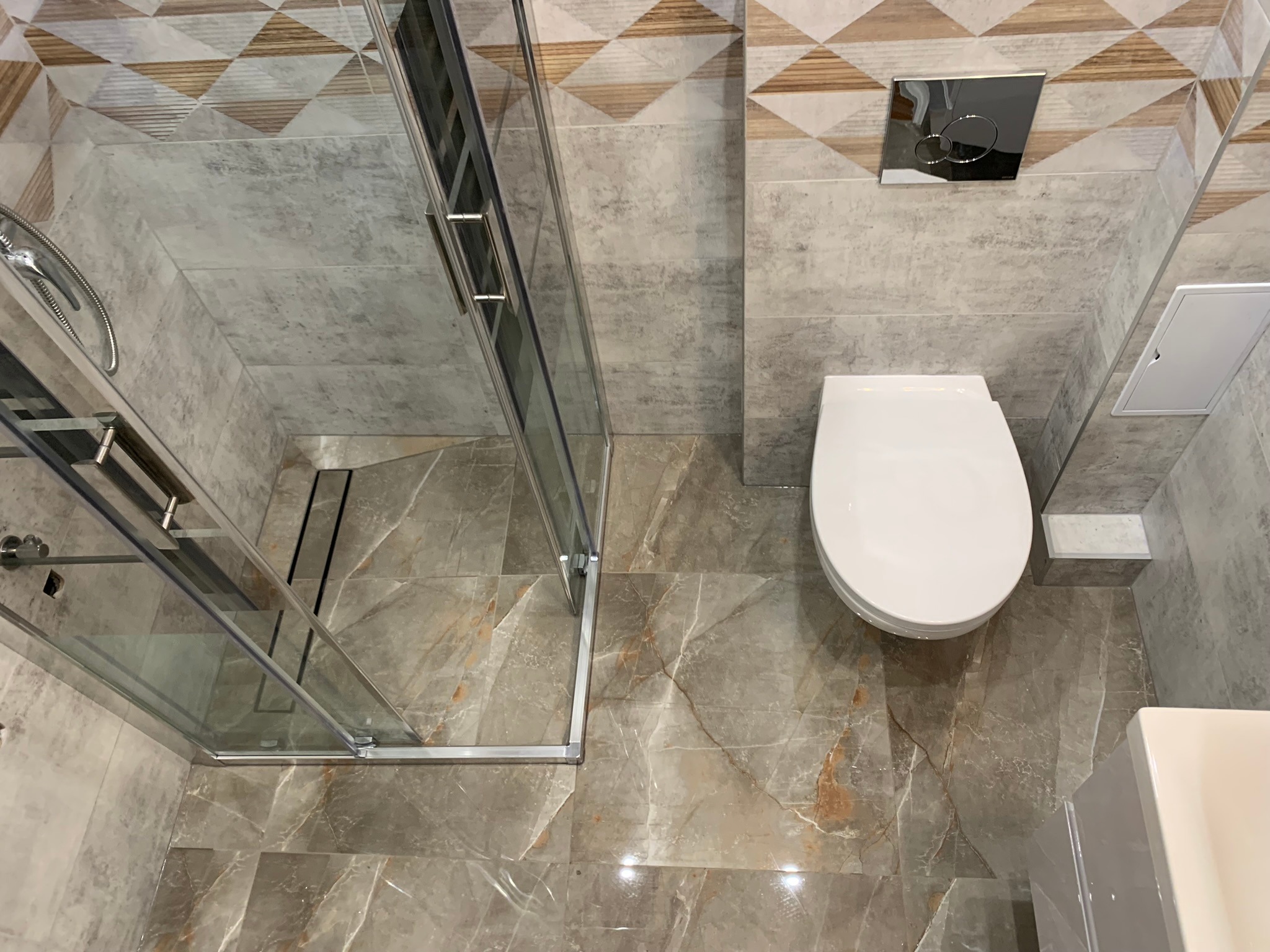 Nowoczesna łazienka z kabiną prysznicową typu walk-in, podwieszaną toaletą i marmurowymi płytkami podłogowymi w odcieniach szarości i beżu, widok z góry.