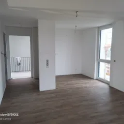 Wnętrze pustego, świeżo wykończonego pokoju w Trzciance z drewnopodobną podłogą, białymi ścianami i widocznymi instalacjami elektrycznymi przed montażem osprzętu.