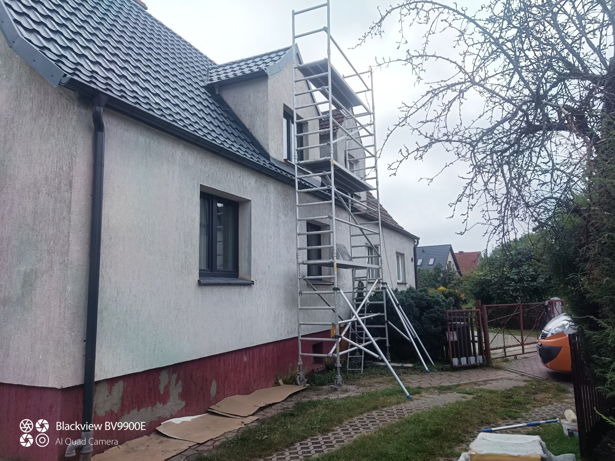 Dom jednorodzinny w trakcie prac elewacyjnych. Widoczne rusztowanie i fragmenty starej powłoki malarskiej. Przygotowania do malowania.