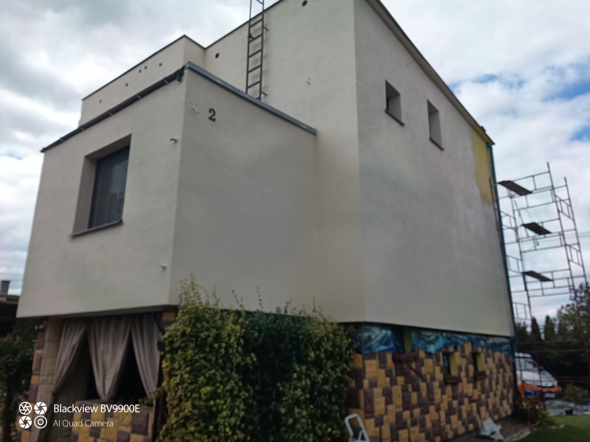 Jasna elewacja domu z numerem 2, częściowo pomalowana na żółto. Widoczne rusztowanie i drabina. Prace w toku, elewacja w trakcie odświeżania.