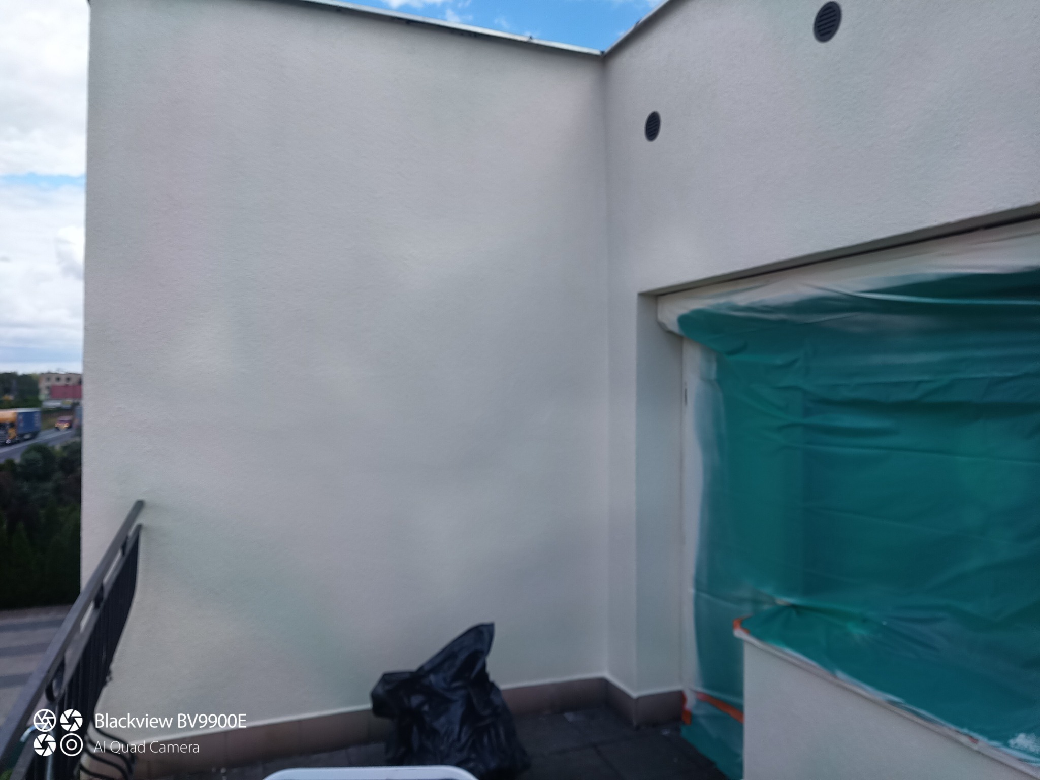 Świeżo pomalowana, biała elewacja balkonu z widocznym czarnym workiem na śmieci i zabezpieczonym folią oknem, detale wykończenia.