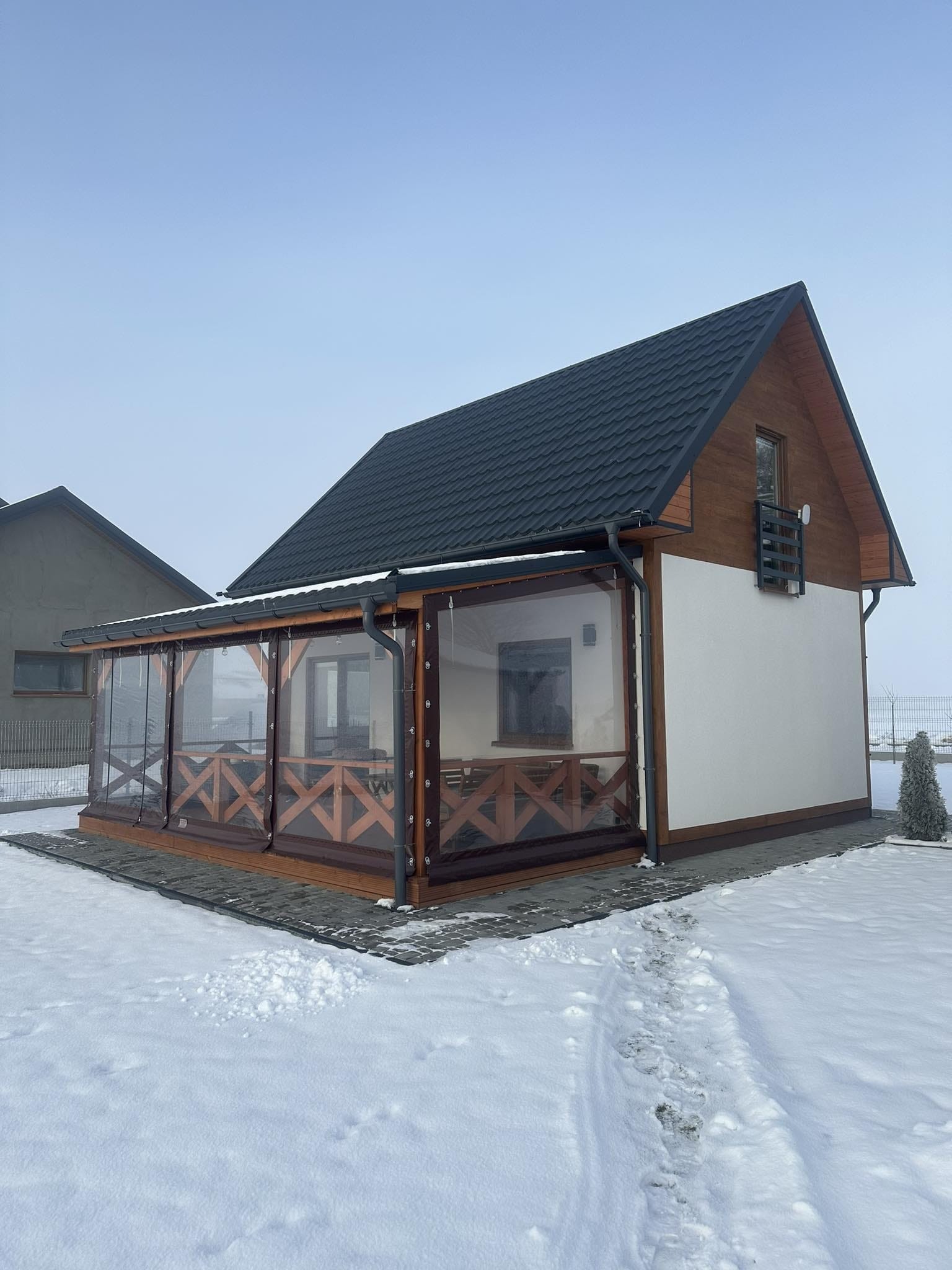 Nowoczesny dom z przeszklonym tarasem i drewnianą konstrukcją, otoczony śniegiem w zimowy dzień.