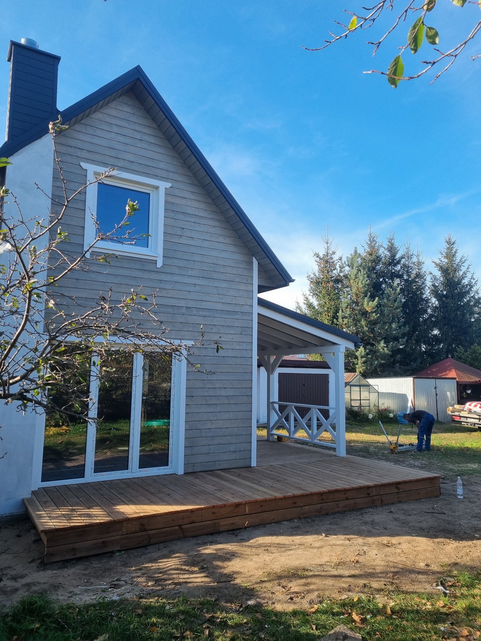 Szary dom z drewnianą elewacją i nowym tarasem w Gdańsku, widok z zewnątrz podczas prac wykończeniowych na posesji.