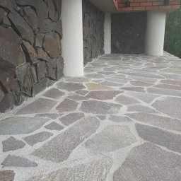 Usługi Remontowo-Budowlane Koza Marek - Kamienna elewacja budynku z nieregularną okładziną i kolumnami, widoczna kamienna posadzka balkonu z szarych płyt o nieregularnych kształtach.