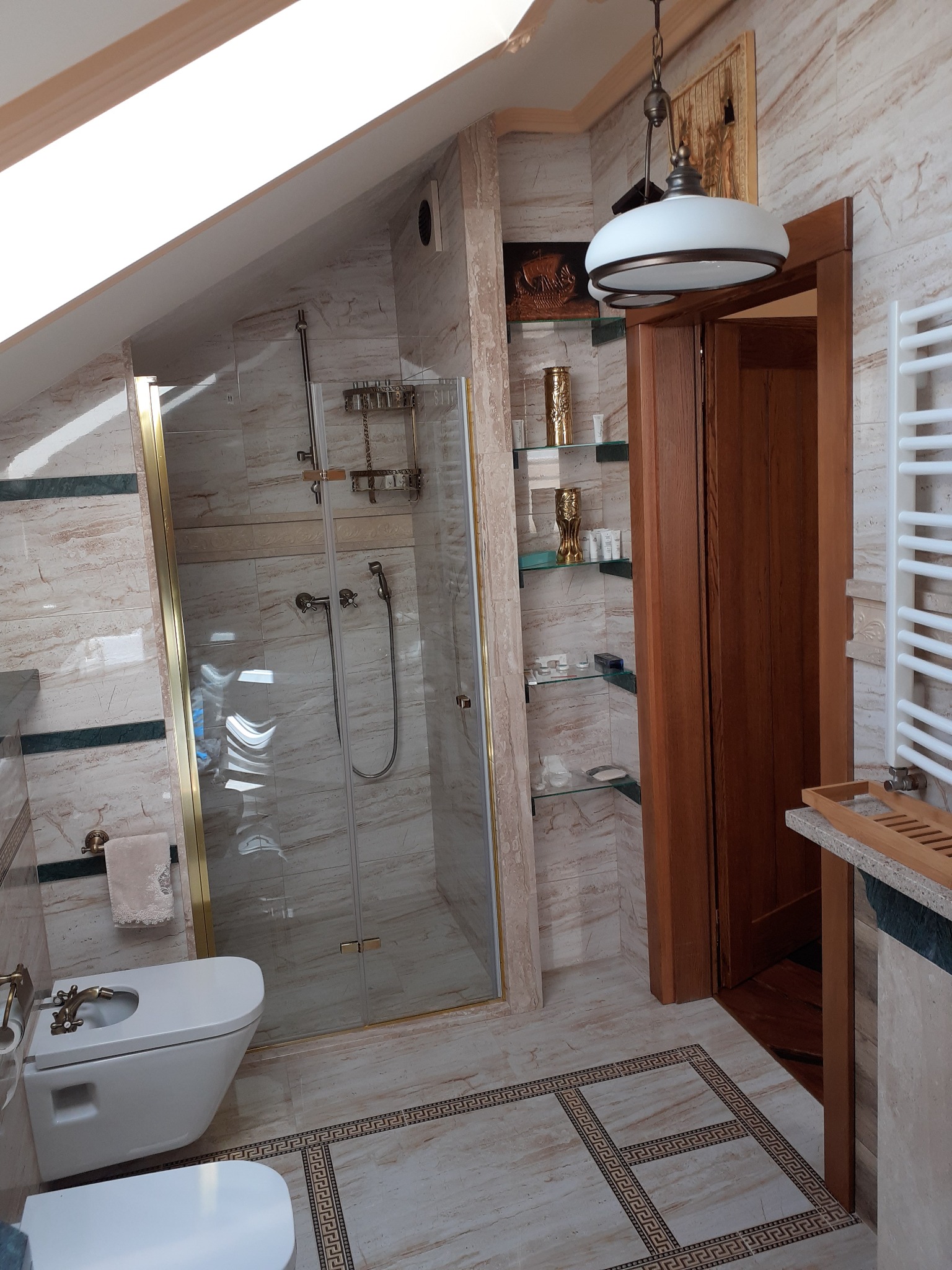 Wykończona łazienka na poddaszu z kabiną prysznicową ze złotymi okuciami, bidetem, grzejnikiem drabinkowym i dekoracyjnymi półkami z oświetleniem.
