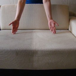 Eco Imperial Cleaning - Jasna kanapa z widoczną różnicą w czystości tapicerki po praniu, z rękami wskazującymi na wyczyszczony obszar.