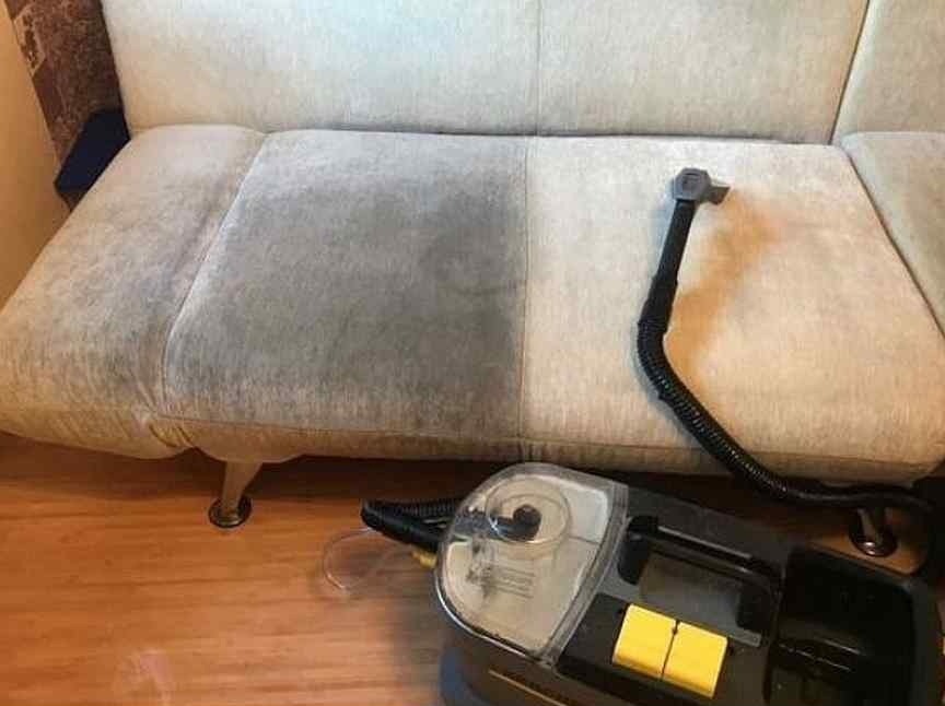 Dwuczęściowa kanapa z widoczną różnicą czystości po lewej i prawej stronie, z czarnym wężem i odkurzaczem do czyszczenia tapicerki na drewnianej podłodze.