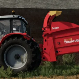Czerwony traktor Massey Ferguson z zamontowanym rozrzutnikiem obornika Teagle Tomahawk 6200H na tle ceglanego budynku.