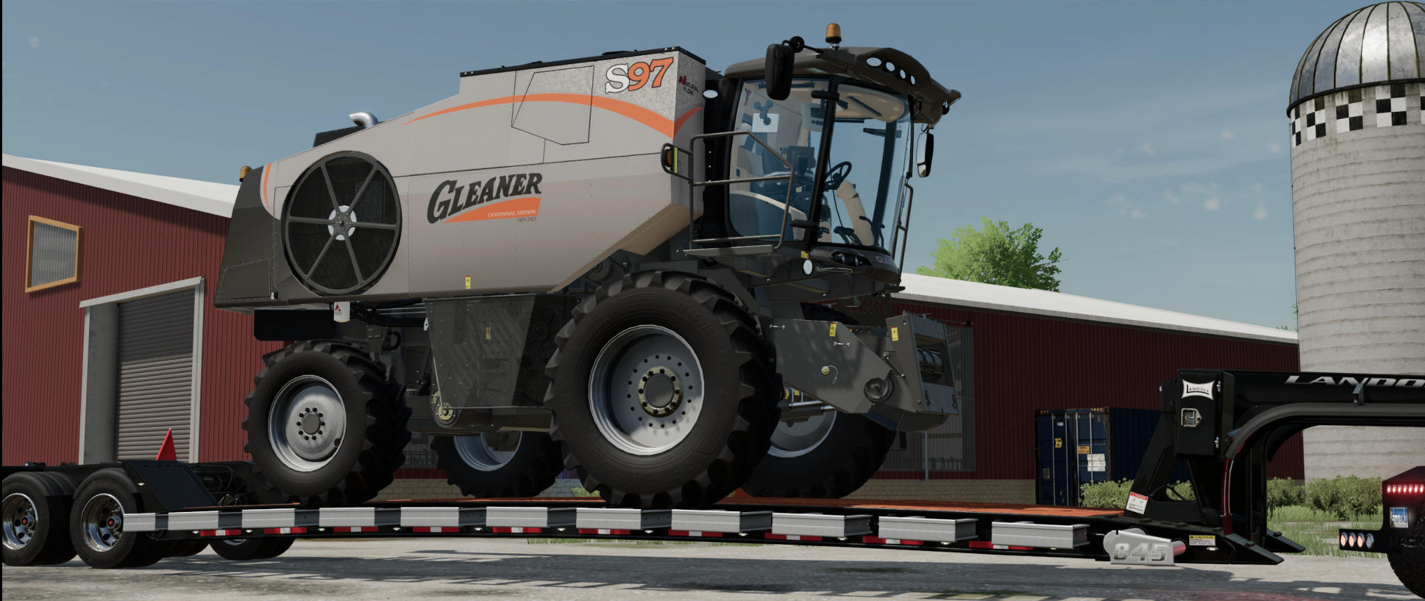 Kombajn zbożowy Gleaner S97 Centennial Edition na niskopodwoziowej przyczepie, z budynkiem gospodarczym i silosem w tle.