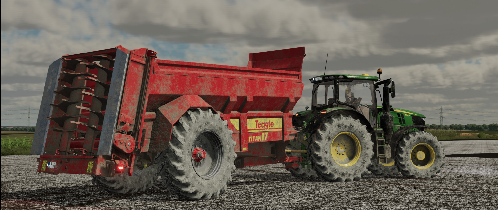 Czerwony rozrzutnik obornika Teagle Titan 17 podłączony do zielonego traktora John Deere na polu w pochmurny dzień.