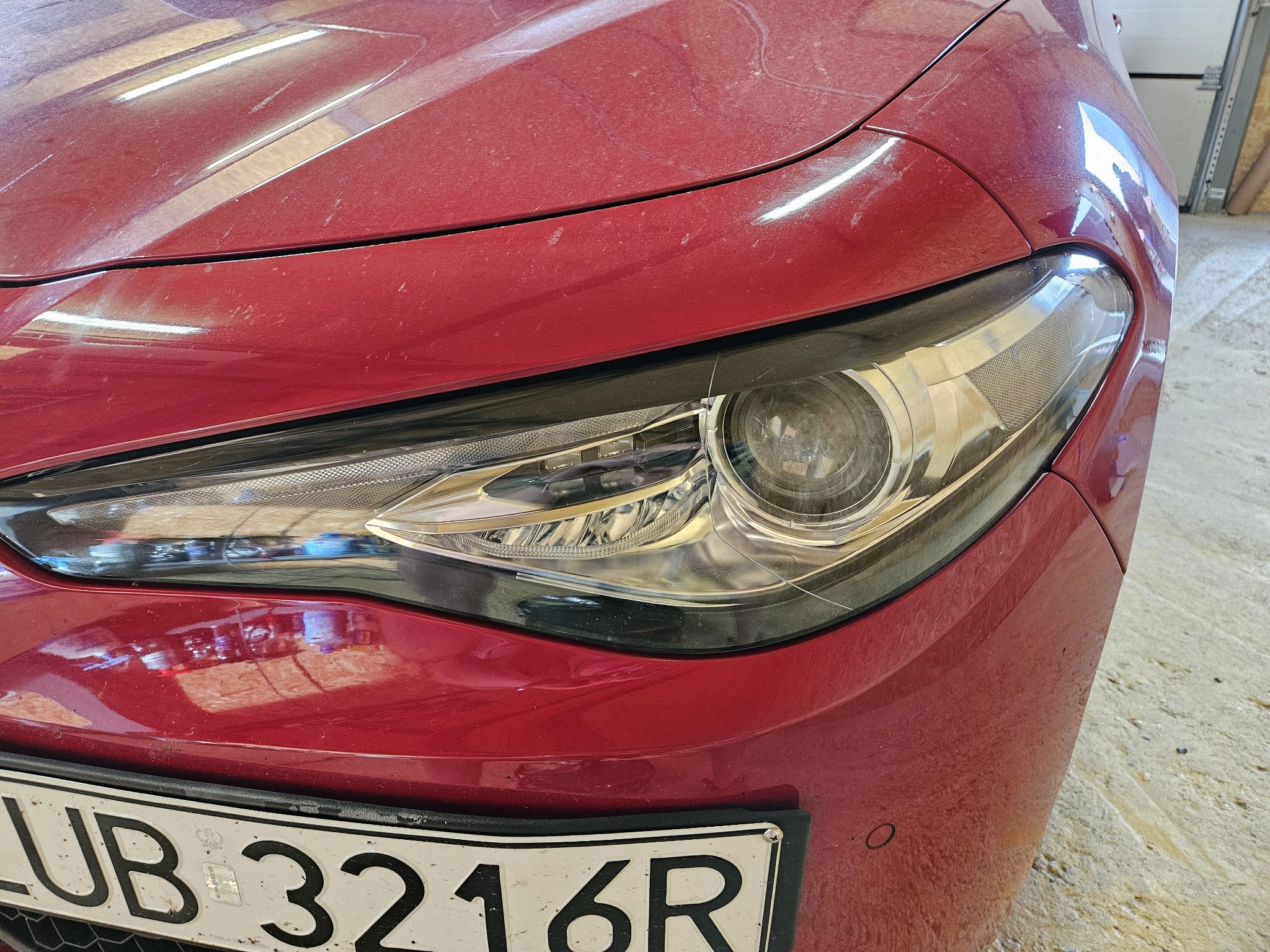 Czerwony samochód Alfa Romeo z widocznym reflektorem i tablicą rejestracyjną; karoseria pokryta warstwą kurzu.