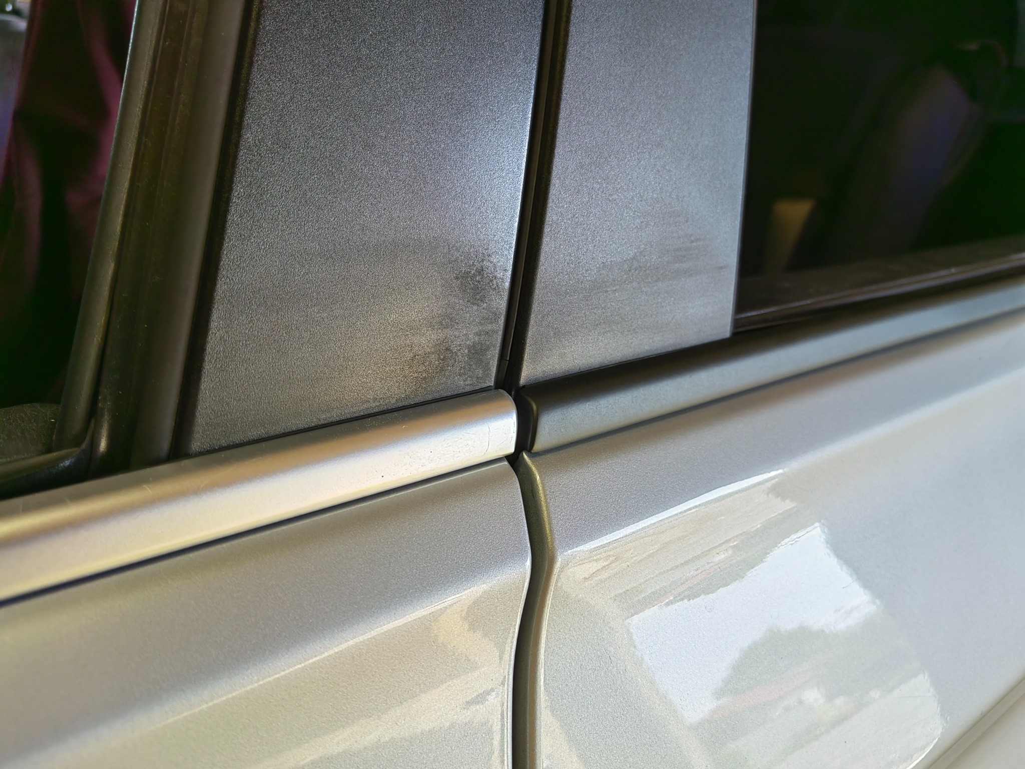 Fragment srebrnego samochodu z widocznym łączeniem drzwi i lekko przyciemnioną szybą boczną, ukazujący różnicę w odcieniach i fakturach materiałów.