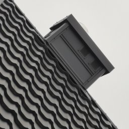 Stanbud - Fragment dachu z czarnej, falistej dachówki ceramicznej i czarnym kominkiem wentylacyjnym z widocznymi kratkami wentylacyjnymi, sfotografowany pod kątem.