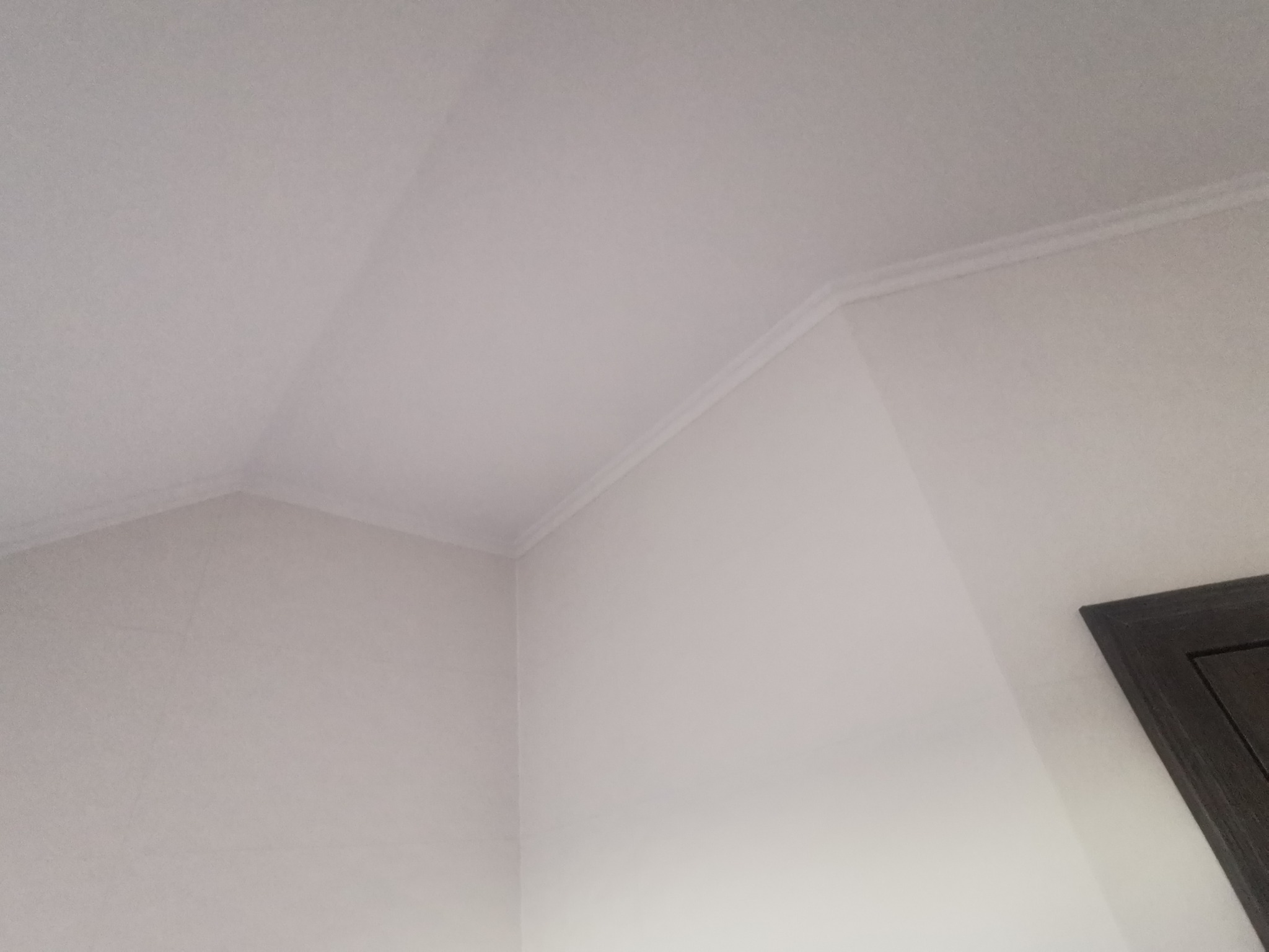 Pomieszczenie po remoncie: białe ściany i sufit z delikatnym sztukateryjnym wykończeniem przy suficie, widoczny fragment ciemnej futryny drzwi.