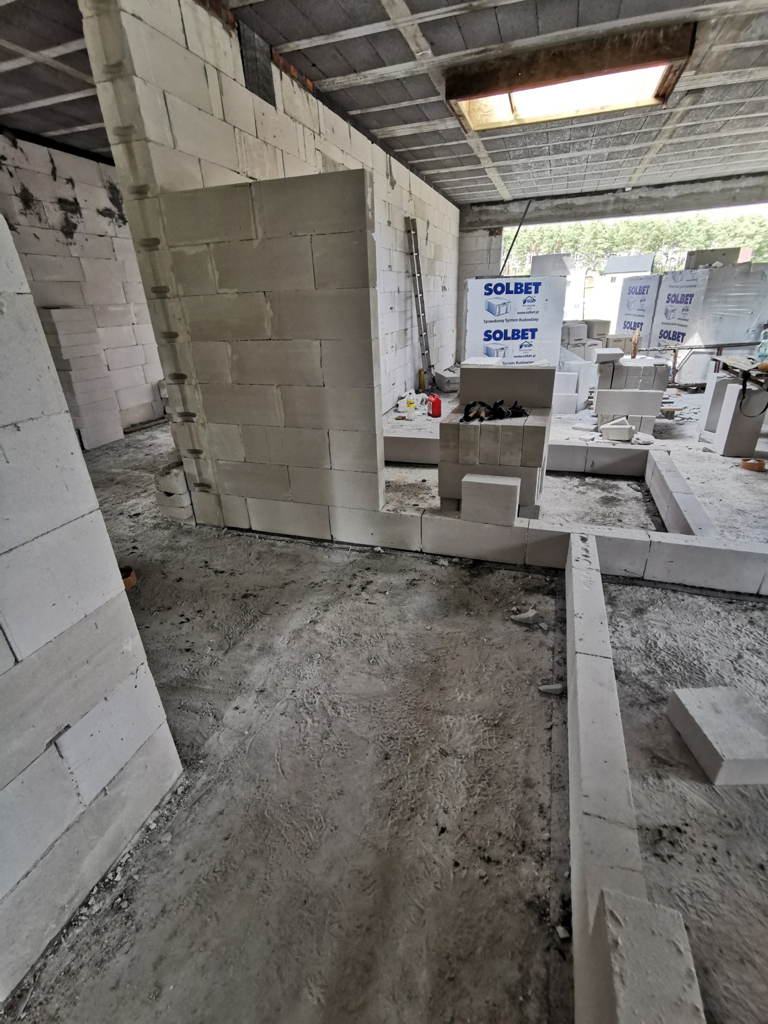 Wnętrze domu w trakcie budowy z betonu komórkowego: wzniesione ściany działowe, fundamenty i palety bloków Solbet w tle.