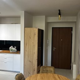 Marcin Szalanski - Nowoczesne wnętrze: biała kuchnia z czarnym panelem, drewniany blat, okrągły stół z krzesłami, drzwi wejściowe i ściana z marmurowym wzorem.