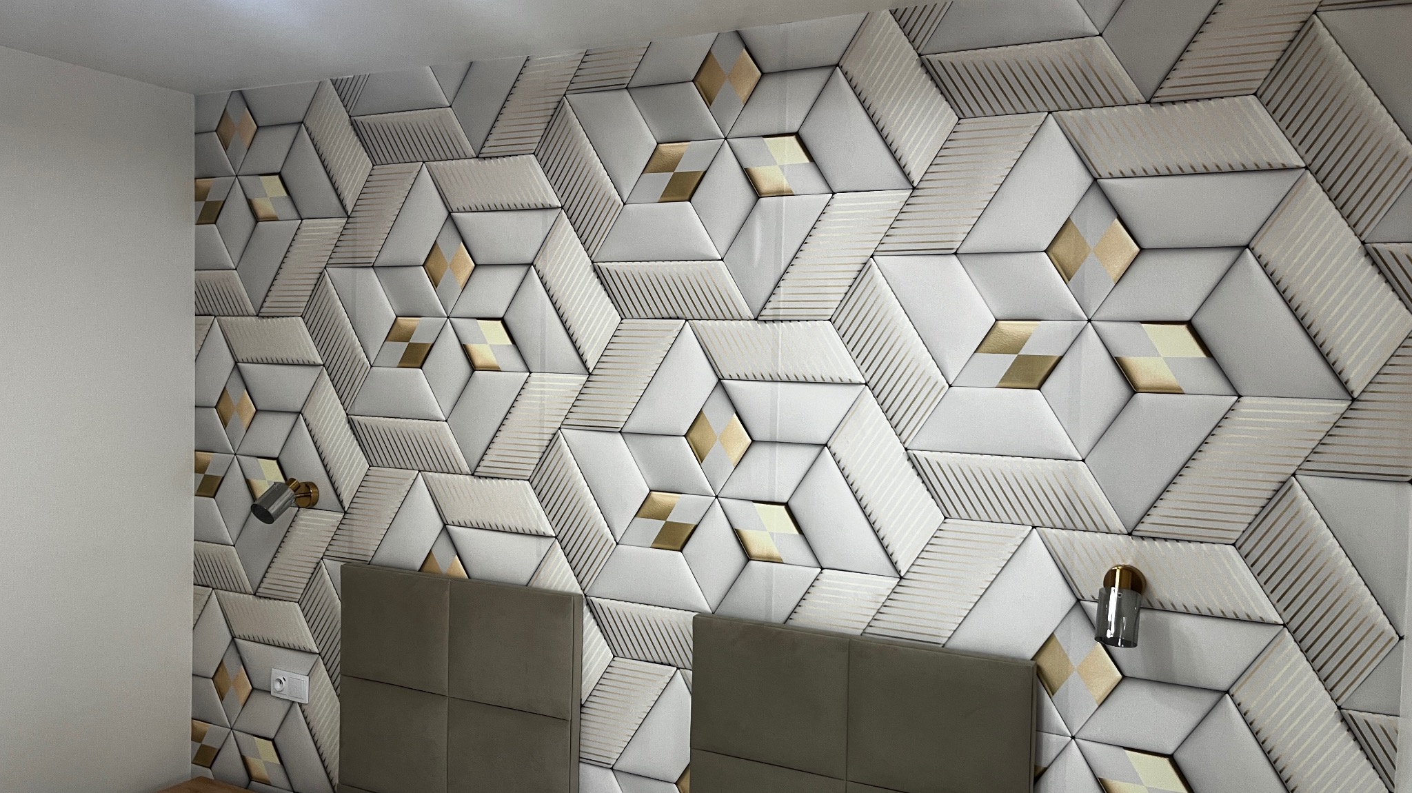 Dekoracyjna ściana z paneli 3D w kształcie rombów i sześciokątów, w odcieniach bieli i złota, nad wezgłowiem łóżka, oświetlona kinkietami.