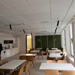 Dmytro Skr - Jasne biuro z białymi stołami, drewnianymi krzesłami, aneksem kuchennym i panelami akustycznymi w odcieniach zieleni.