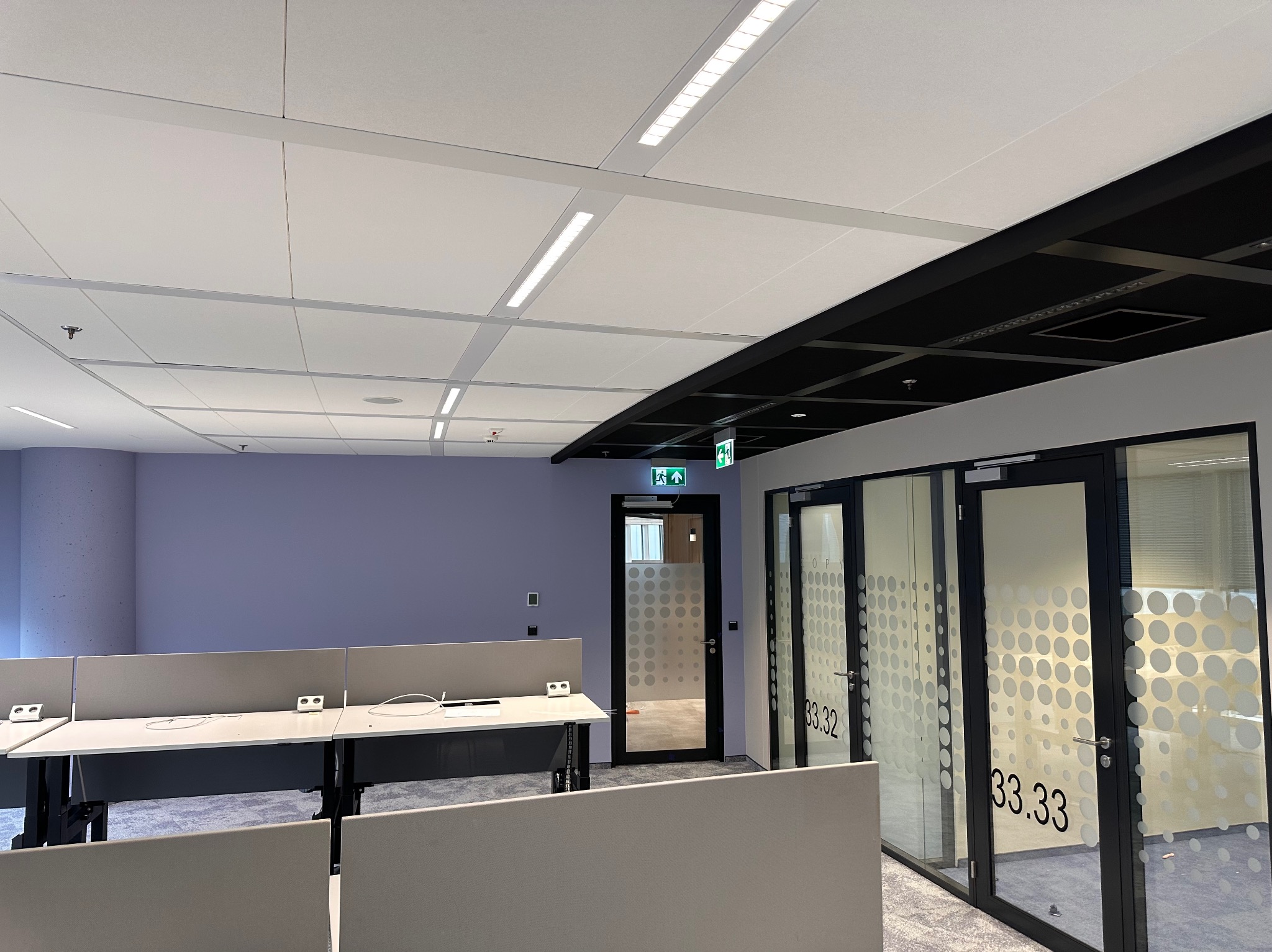 Wykończone wnętrze biurowe z biurkami, przeszklonymi drzwiami z numerami pokoi i podwieszanym sufitem z oświetleniem LED.
